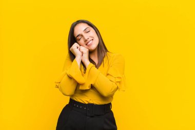 Genç, güzel bir kadın aşık ve sevimli görünüyor. Sevimli ve mutlu. Elleri turuncu duvarın yanında, romantik bir şekilde gülümsüyor.