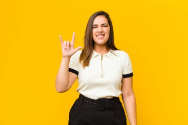 Genç, güzel bir kadın kendini mutlu, eğlenceli, kendinden emin, pozitif ve isyankar hissediyor. Turuncu duvarda elle izole edilmiş kaya ya da heavy metal tabelaları yapıyor.