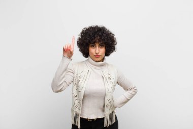 Genç, güzel afro kadın mutlu bir şekilde gülümsüyor, tek eliyle uzayı işaret ediyor.