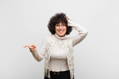 Genç, güzel afro kadın gülüyor, mutlu, pozitif ve şaşırmış görünüyor, yanal fotokopi alanını işaret eden harika bir fikri fark ediyor.