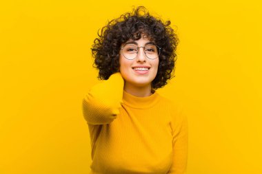 Genç, güzel afro kadın neşeli ve kendinden emin bir şekilde gülüyor, mutlu, dostane bir gülümsemeyle.