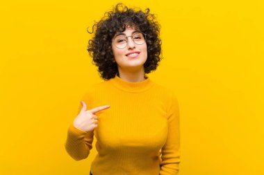 Genç, güzel afro kadın gururlu, kendinden emin ve mutlu görünüyor, gülümsüyor ve kendini işaret ediyor ya da bir numaralı işareti yapıyor.