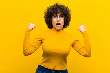 Genç, güzel afro kadın sinirli bir ifadeyle bağırıyor ya da yumruklarıyla başarıyı kutluyor.