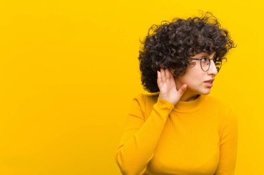 Genç, güzel afro kadın ciddi ve meraklı görünüyor, dinliyor, gizli bir konuşma veya dedikodu duymaya çalışıyor, gizlice dinliyor.