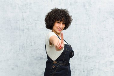 Genç, güzel afro kadın gururla gülümsüyor ve gururla bir numaralı pozunu veriyor, kendini lider gibi hissediyor.