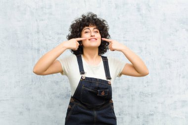 Genç, güzel afro kadın, kendine güvenerek gülümsüyor. Geniş bir gülümseme, pozitif, rahat, tatmin olmuş bir tavır sergiliyor.