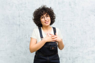Genç, güzel afro kadın romantik, mutlu ve aşık, neşeyle gülümsüyor ve kalbe yakın el ele tutuşuyor.