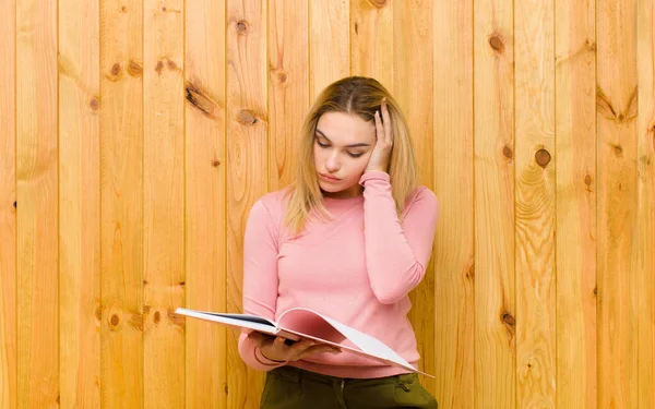 young pretty blonde woman with books against wood wall