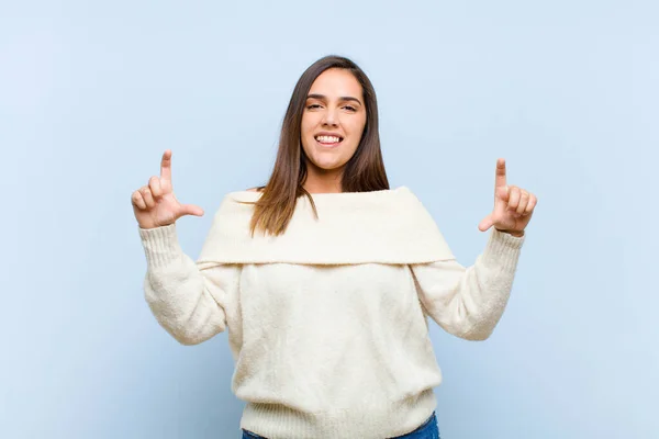 young pretty woman framing or outlining own smile with both hands, looking positive and happy, wellness concept against blue background