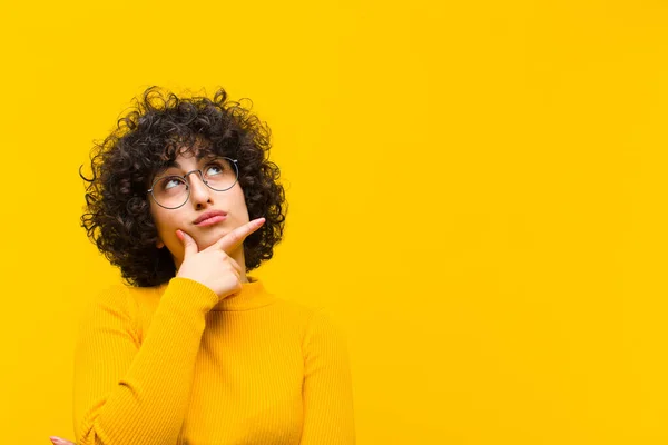 young pretty afro woman feeling thoughtful, wondering or imagining ideas, daydreaming and looking up to copy space