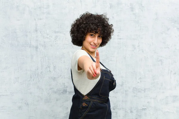 Genç, güzel afro kadın gururla gülümsüyor ve gururla bir numaralı pozunu veriyor, kendini lider gibi hissediyor.