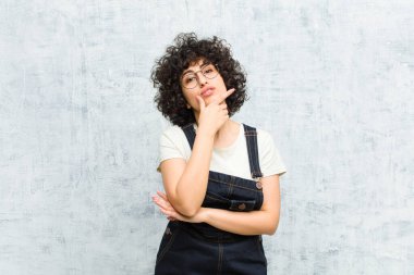 Genç, güzel afro kadın ciddi, düşünceli ve güvensiz görünüyor, bir kolu çapraz ve çene üzerinde, seçenekleri tartıyor