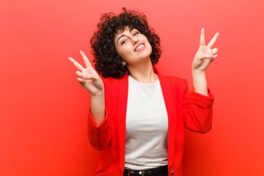 Genç ve güzel afro kadın gülümsüyor ve mutlu görünüyor, arkadaş canlısı ve tatmin olmuş, zafer ya da barış işareti yapıyor.