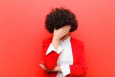 Genç, güzel afro kadın stresli, utanmış ya da üzgün görünüyor, baş ağrısı var, yüzünü eliyle kapatıyor.