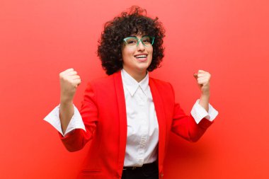 Genç ve güzel bir afro kadın mutlu, şaşırmış ve gururlanmış hissediyor, bağırıyor ve başarıyı büyük bir gülümsemeyle kutluyor.