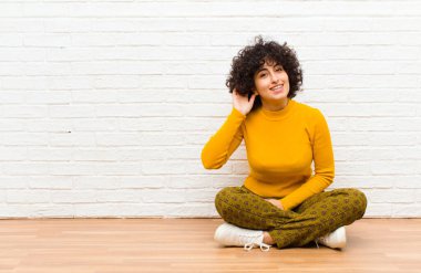 Genç, güzel afro kadın gülümsüyor, tuhaf bir şekilde yan tarafa bakıyor, yerde oturan bir sırrı dinlemeye çalışıyor.