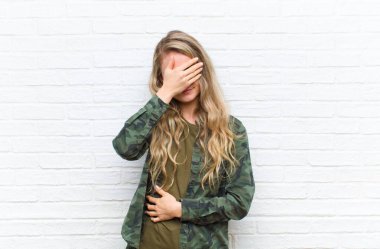 Genç sarışın kadın stresli, utanmış ya da üzgün görünüyordu, baş ağrısı vardı, yüzünü tuğla duvara dayamıştı.