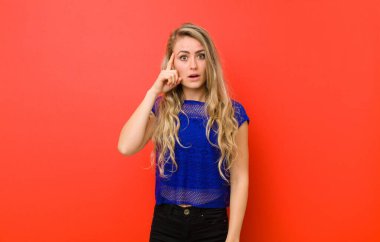 Genç sarışın kadın şaşırmış, ağzı açık, şok olmuş, kırmızı duvara karşı yeni bir düşünce, fikir ya da konsept fark ediyor.