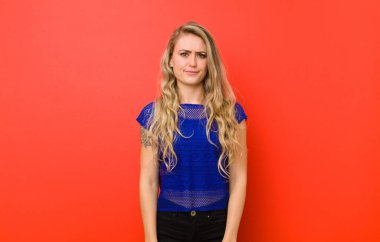 şaşkın ve şüpheli, merak veya seçmeye veya kırmızı duvara bir karar vermeye çalışan genç sarışın kadın