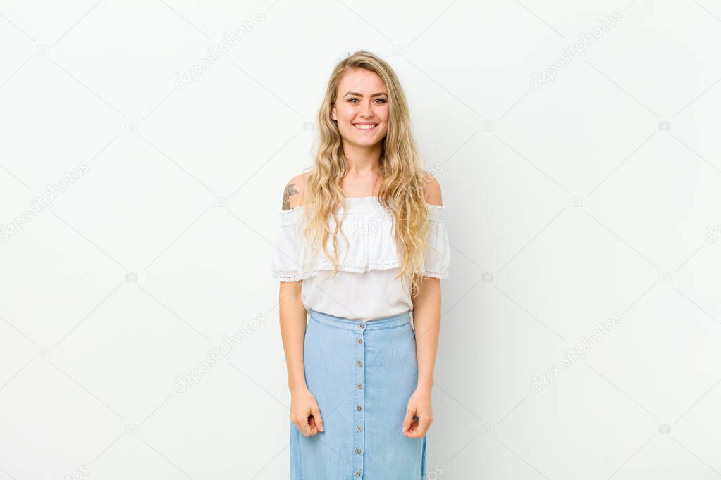 young blonde woman looking happy and goofy with a broad, fun, loony smile and eyes wide open against white wall