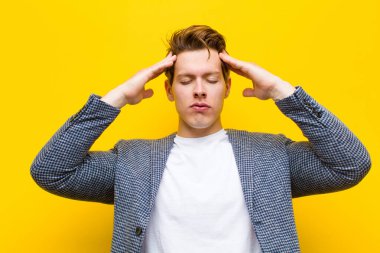 Genç kızıl saçlı adam konsantre, düşünceli ve ilham verici görünüyor, beyin fırtınası yapıyor ve turuncu arka planda elleri alnında hayal ediyor.