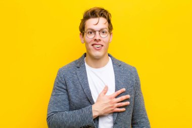 Genç kızıl saçlı adam şaşkın ve şaşırmış hissediyor, gülümsüyor, el ele tutuşuyor, mutlu ya da turuncu arka plana karşı minnettarlık gösteriyor.