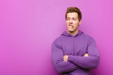 Genç kızıl saçlı adam şüphe ediyor ya da düşünüyor, dudağını ısırıyor ve kendini güvensiz ve gergin hissediyor, mor duvara karşı boşluğu kopyalamak istiyor.