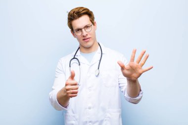 Genç kızıl saçlı doktor gülümsüyor ve arkadaş canlısı görünüyor. 6 ya da 6 numarayı gösteriyor. Elleri önde, mavi duvara doğru sayıyor.