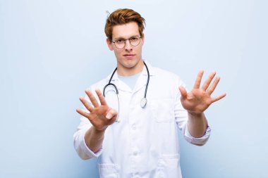 Genç kızıl saçlı doktor gülümsüyor ve dost canlısı görünüyor. 9 ya da 9 numarayı gösteriyor. Eli önde, mavi duvara doğru sayıyor.