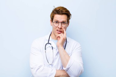 Genç kızıl saçlı doktor şok ve inançsızlıkla ağzı açık, elleri yanak ve kolları çaprazlanmış, sersemlemiş ve mavi duvara karşı şaşkın hissediyordu.