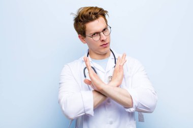 Genç kızıl saçlı doktor senin tavırlarından rahatsız ve bıkkın görünüyor, yeter! Eller önde çapraz, mavi duvara yaslanmanı söylüyor.