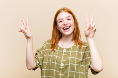Genç kızıl saçlı güzel bir kadın gülümsüyor ve mutlu görünüyor, arkadaş canlısı ve tatmin olmuş, zafer ya da barış işareti yapıyor.