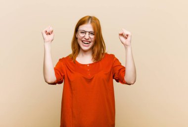 Genç kızıl saçlı güzel kadın mutlu, pozitif ve başarılı hissediyor, zaferi, başarıları ya da iyi şansı kutluyor.