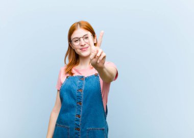 Genç kızıl saçlı güzel bir kadın gülümsüyor ve arkadaş canlısı görünüyor, iki ya da iki numarayı gösteriyor, eli önde, geriye doğru sayıyor.