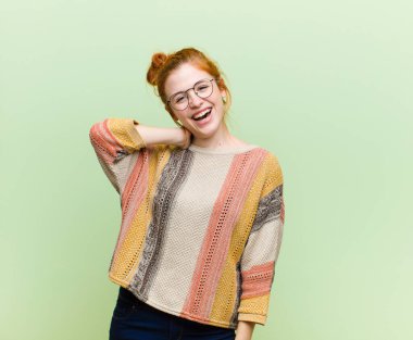 Genç, güzel, kızıl saçlı, neşeli ve kendinden emin bir şekilde gülen bir kadın. Yeşil duvara karşı gülen, mutlu, dostane bir gülümseme.