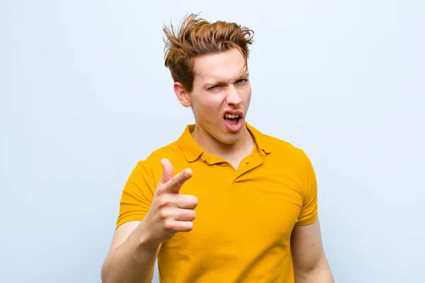 若い赤い頭の男がカメラを指差す怒りの攻撃的な表情青い壁に対して激怒した狂気のボスのように見える — ストック写真