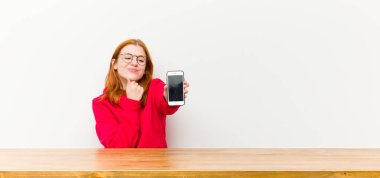 Genç kızıl saçlı güzel bir kadın ahşap bir masanın önünde cep telefonuyla.