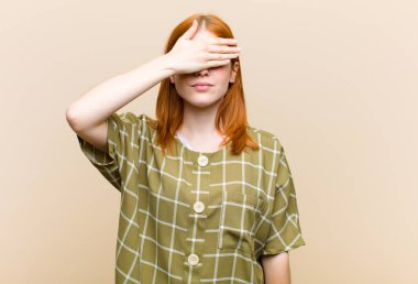 Genç kızıl saçlı güzel bir kadın tek eliyle gözlerini kapatıyor korkmuş ya da endişeli hissediyor, merak ediyor ya da körü körüne bir sürpriz bekliyor.