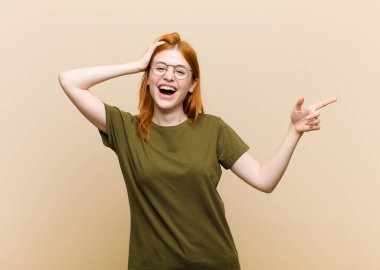 Genç kızıl saçlı güzel kadın gülüyor, mutlu, pozitif ve şaşırmış görünüyor, yanal fotokopi alanını işaret eden harika bir fikrin farkına varıyor.