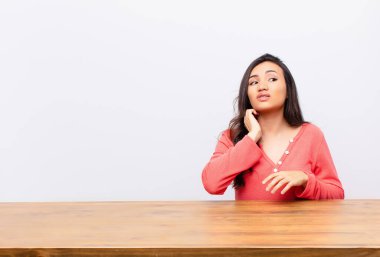 Genç, Latin, güzel bir kadın stresli, hayal kırıklığına uğramış ve yorgun, ağrılı boynu ovuyor, endişeli ve sorunlu bir şekilde düz duvara bakıyor.