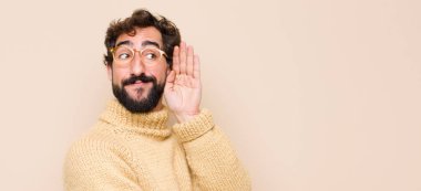 Genç, havalı bir adam gülümsüyor, tuhaf bir şekilde yan tarafa bakıyor, dedikoduları dinlemeye çalışıyor ya da düz duvara karşı bir sırrı duymaya çalışıyor.