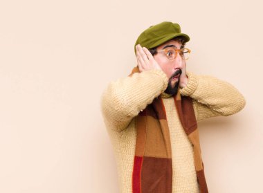 Genç havalı sakallı adam hoş olmayan bir şekilde şok olmuş, korkmuş ya da endişeli görünüyor ağzı sonuna kadar açık ve iki kulağını da elleriyle kapatıyor.