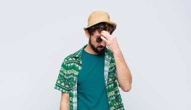 Genç turist stresli, mutsuz ve hayal kırıklığına uğramış hissediyor, alnına dokunuyor ve beyaz duvara karşı şiddetli baş ağrısı çekiyor.