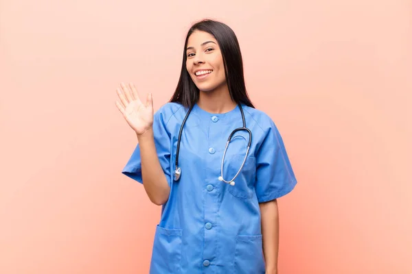 若いラテン語の看護師は喜んで明るく手を振ってあなたを歓迎し挨拶したりピンクの壁にさよならを言う — ストック写真