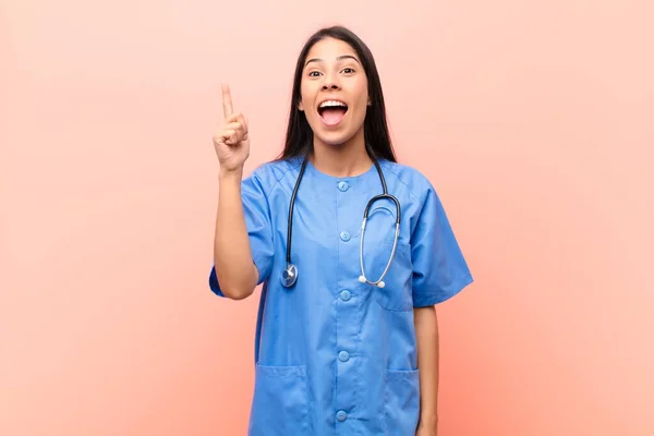 若いラテン語の看護師はアイデアを実現した後 幸せで興奮した天才のように感じ 陽気に指を上げる ユーレカ ピンクの壁に — ストック写真