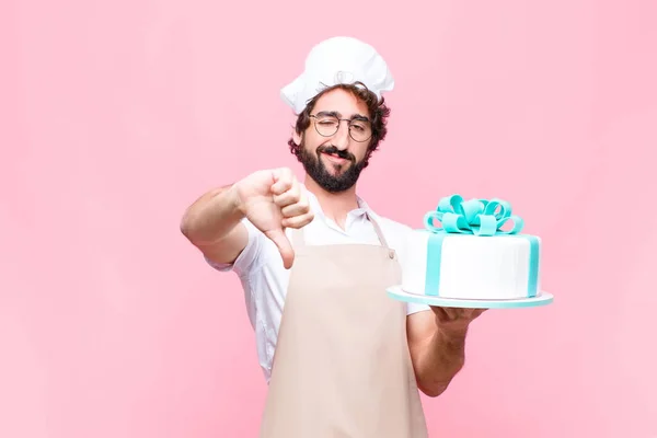young crazy baker man holding a cake against pink wall