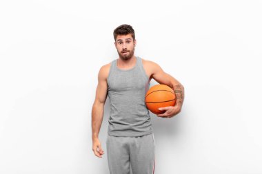 Şaşkın ve kafası karışmış genç bir adam gergin bir hareketle dudağını ısırıyor basketbol topu tutan sorunun cevabını bilmiyor..