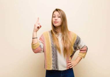 Genç sarışın kadın, harika bir fikrin farkına vardıktan sonra parmağını gururla havada tutan bir dahi gibi hissediyor. Bej duvara karşı 