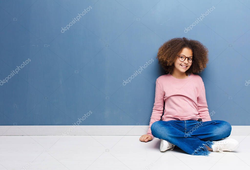 african american little girl with a big, friendly, carefree smile, looking positive, relaxed and happy, chilling sitting on the floor