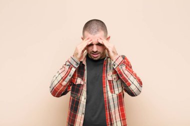 Genç ve yakışıklı bir adam stresli ve hayal kırıklığına uğramış görünüyor. Baskı altında, baş ağrısı ve düz duvara karşı sorunlarla çalışıyor.